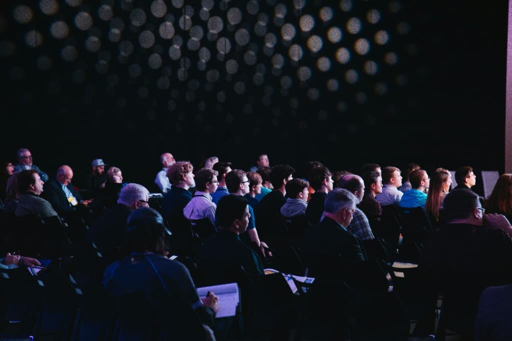 Pubblico attento in sala durante un evento di comunicazione aziendale, a rappresentare allineamento e valore condiviso